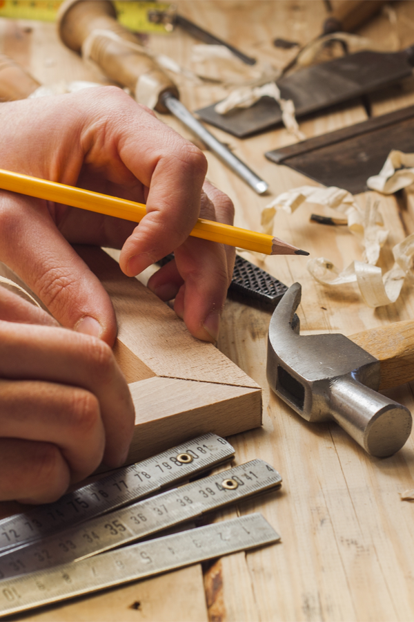 close up of a person holding wooden corner ends on a wooden table, along with tools and wooden scraps strewn about on the table